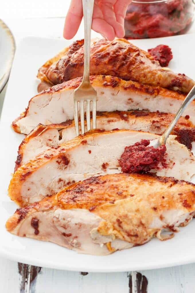 Roasted Cranberry Butter Turkey sliced on white tray with fork held by hand and spoon with cranberry butter