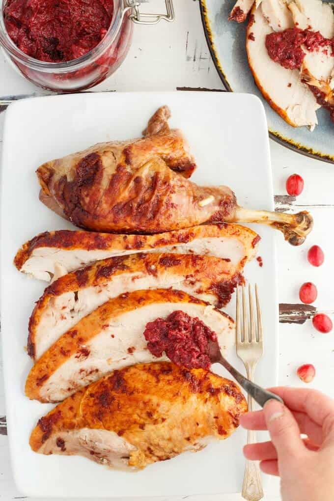 Roasted Cranberry Butter Turkey slices and thigh on white tray with fork and spoon full of butter held by hand