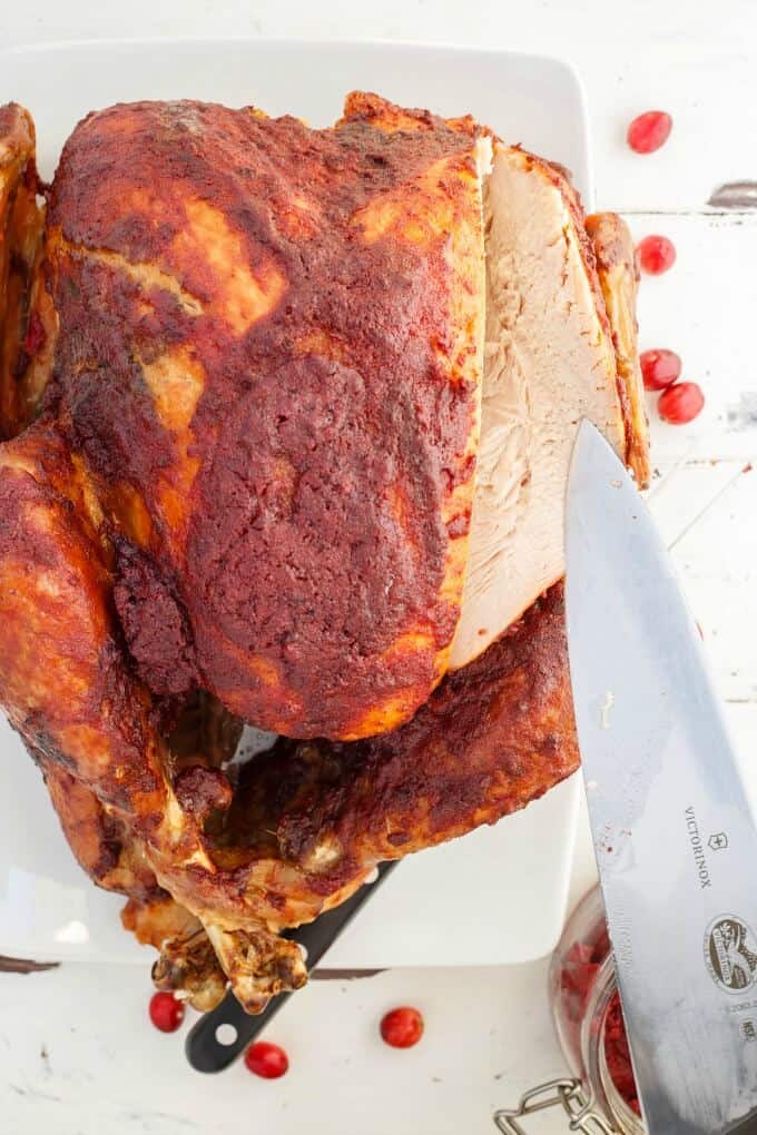 Roasted Cranberry Butter Turkey on white tray with knife, scattered cranberries and jar of butter