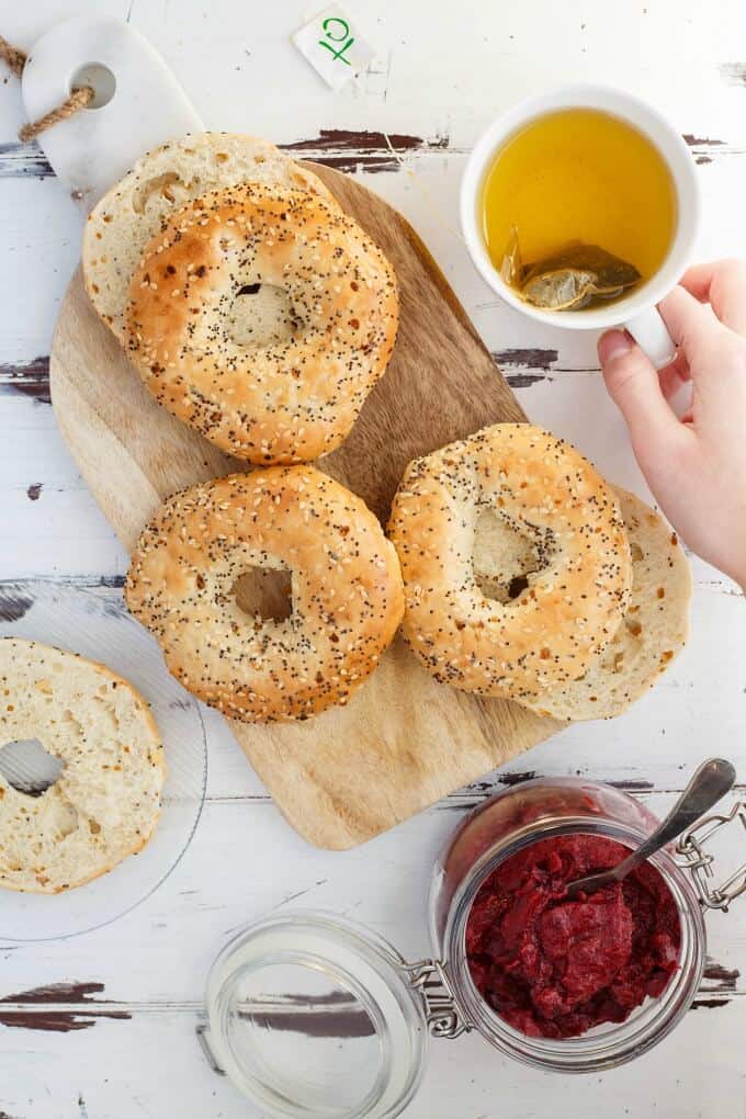 Slow Cooker Cranberry Butter in glass jar with spoon next to doughnuts on wooden pad with cup of tea held by hand(Vegan/GF)