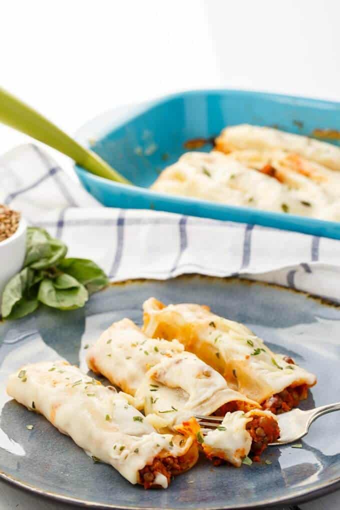 Turkey-Lentil Cannelloni  on gray tray with fork, in blue casserole with green spatula in the background