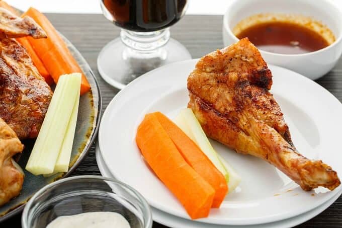 Zesty Maple Turkey Wings on blue tray and white plate with vegetable, bowl of sauce with glass cup and small glass bowl on table