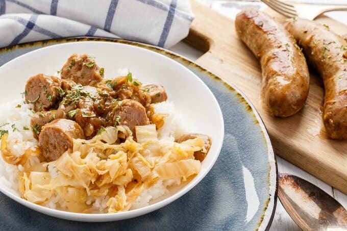 Beer Gravy Sausage Dinner on white plate next to spoon and wooden pad with sausages