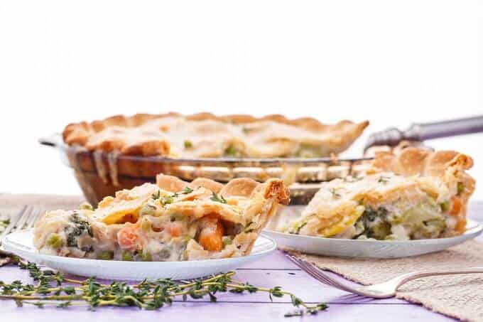 Hearty Vegetarian Pot Pie on white plates with herbs and fork on purple table. Rest of cake in pot in the background
