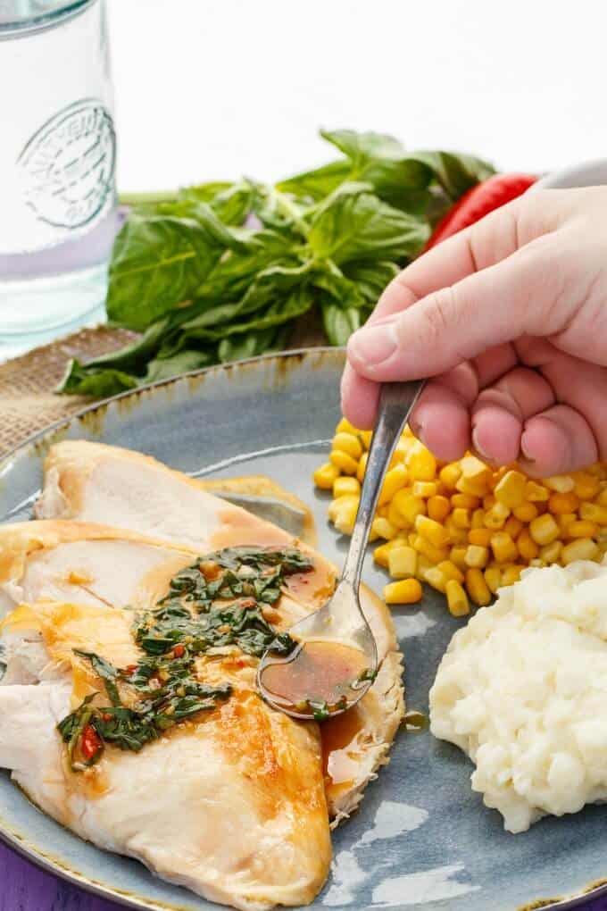 Inauthentic Thai Basil Turkey  on blue table with spoon held by hand with corn, mashed potatoes. Herbs and glass cup in the background