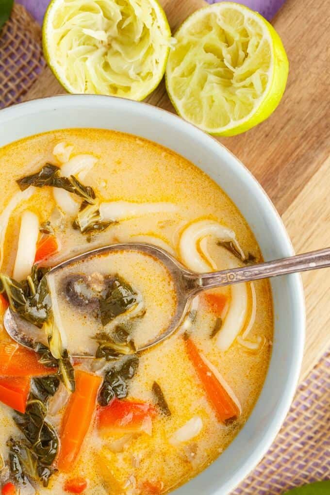 Inauthentic Vegetarian Thai Basil Soup in white bowl with spoon on wooden pad with lemon sliced in half