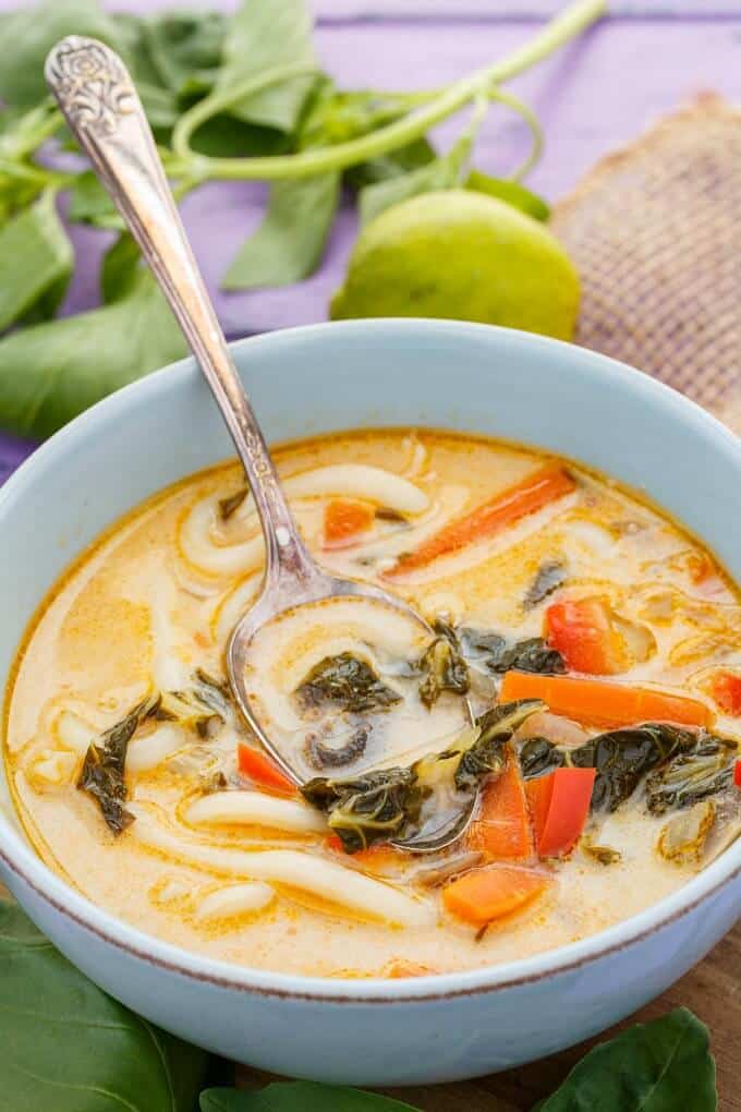 Inauthentic Vegetarian Thai Basil Soup in white bowl with spoon, Lemon, herbs on purple table