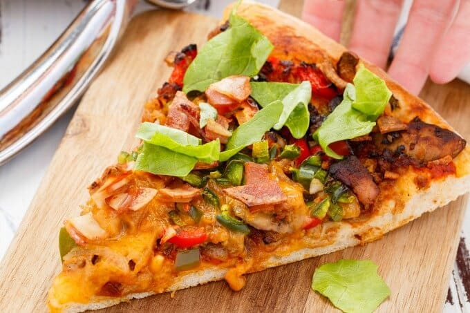 Turkey Bacon Cheeseburger Pizza slice on wooden tray touched by hand