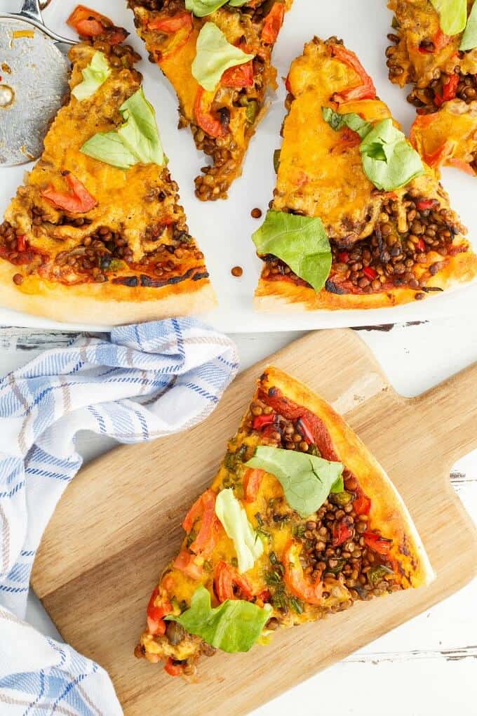 Vegetarian Lentil Cheeseburger Pizza slices on white tray and wooden pad next to cloth wipe