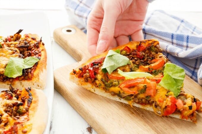 Vegetarian Lentil Cheeseburger Pizza on white pad touched by hand  and on white tray