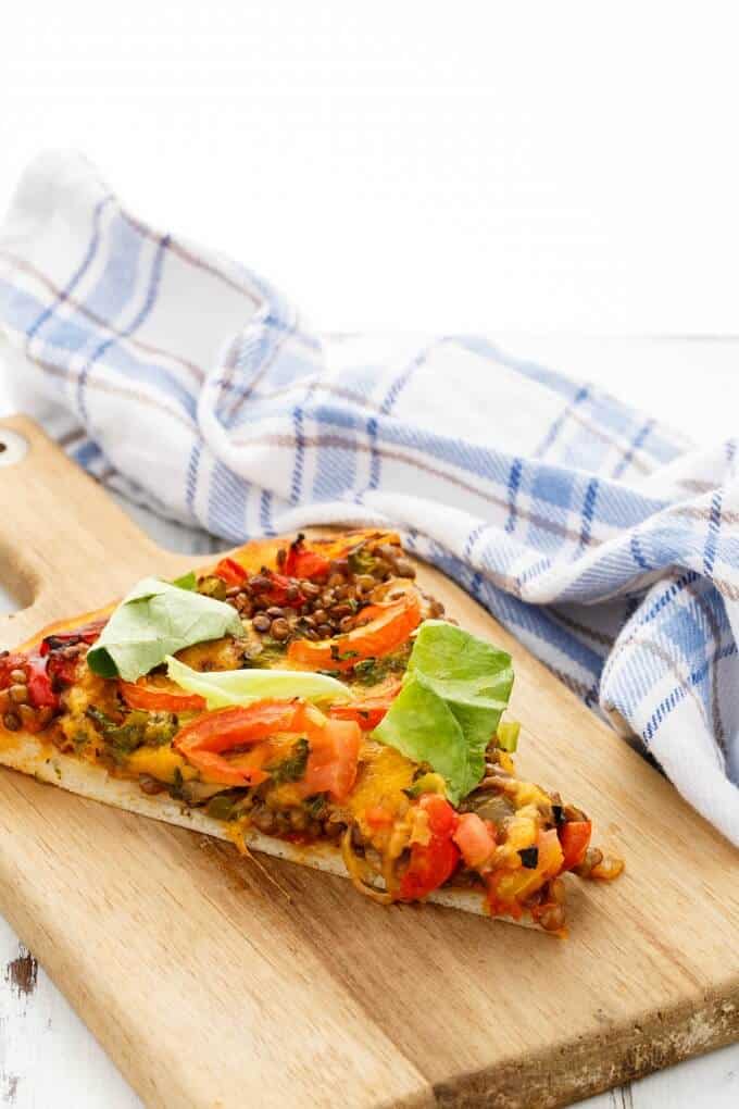 Vegetarian Lentil Cheeseburger Pizza slice on wooden pad next to cloth wipe