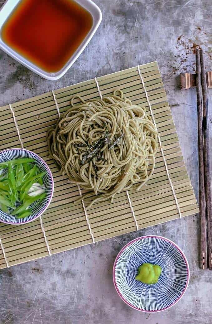 Zaru soba noodles on wooden pad with bowls of vegetable, butter and sauce