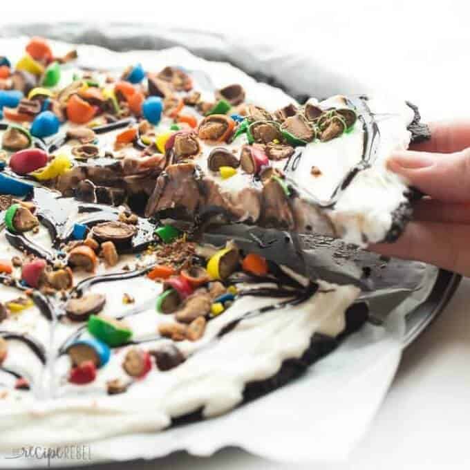 Frozen ice cream dessert pizza on silver tray, one slice held by hand