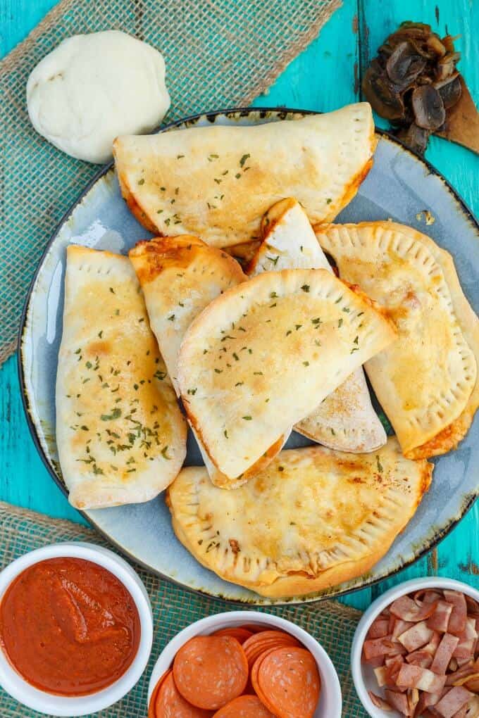 Homemade Pizza Pockets  on blue tray. Bowls of ingredients, pizza dough, spatula with mushrooms on blue table