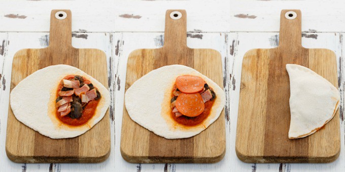 Homemade Pizza Pockets rolled dough on wooden pad being topped.