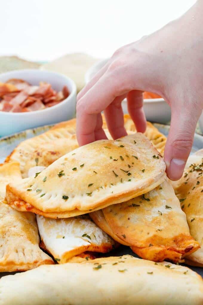 Homemade Pizza Pockets  on gray tray , pocket touched by hand, bowls of ingredients in the background