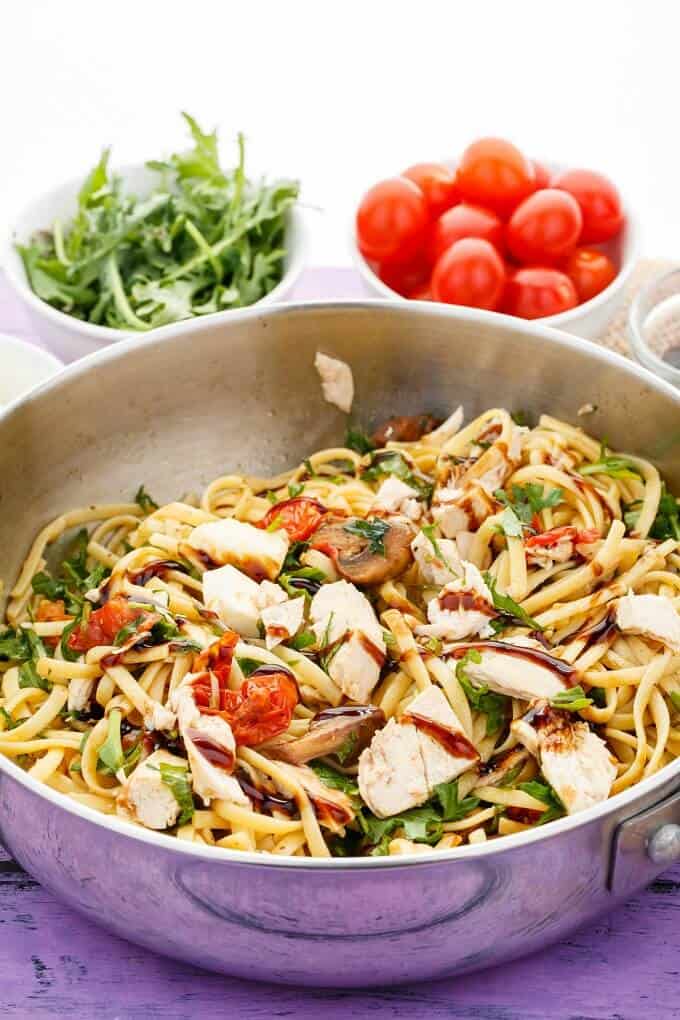 Roasted Chicken Caprese Pasta in pan, bowls of herbs and tomatoes in the background