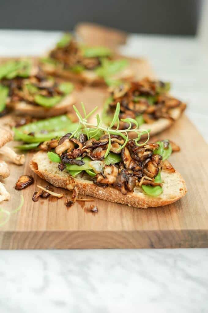 Roasted mushrooms, onion and snow pea crostini on wooden pad