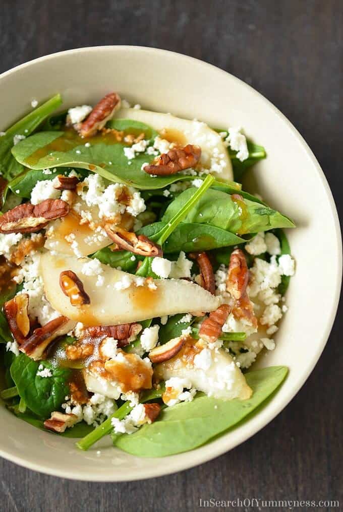 Spinach salad with pears, pecans and goat cheese in white bowl