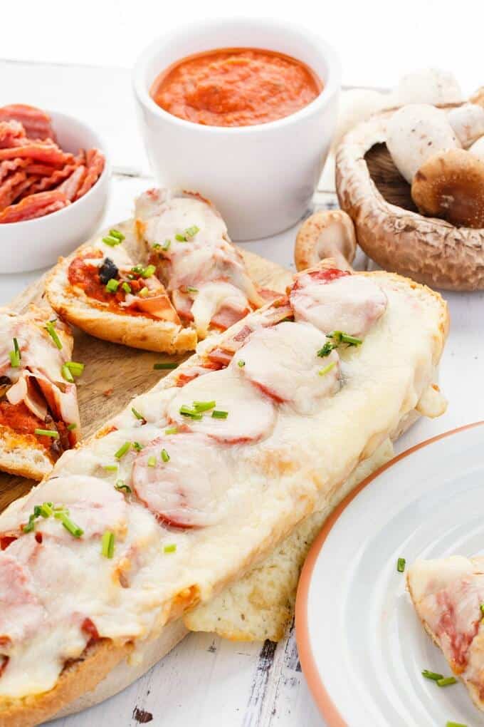 Turkey Pizza Bread  on wooden pad and white plate. Bow of sliced turkey, bowl of sauce and mushrooms on white table