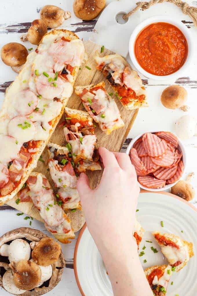 Turkey Pizza Bread  on wooden pad, one slice held by hand. On white plate with bowl of sliced turkey, bowls of sace and mushrooms in table