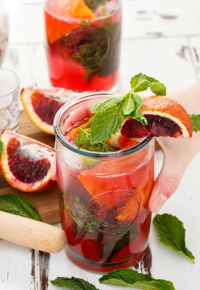 Blood Orange Mojitos in glass cups with herbs, bloodoranges, wooden pad and wooden kitchen tool on the table