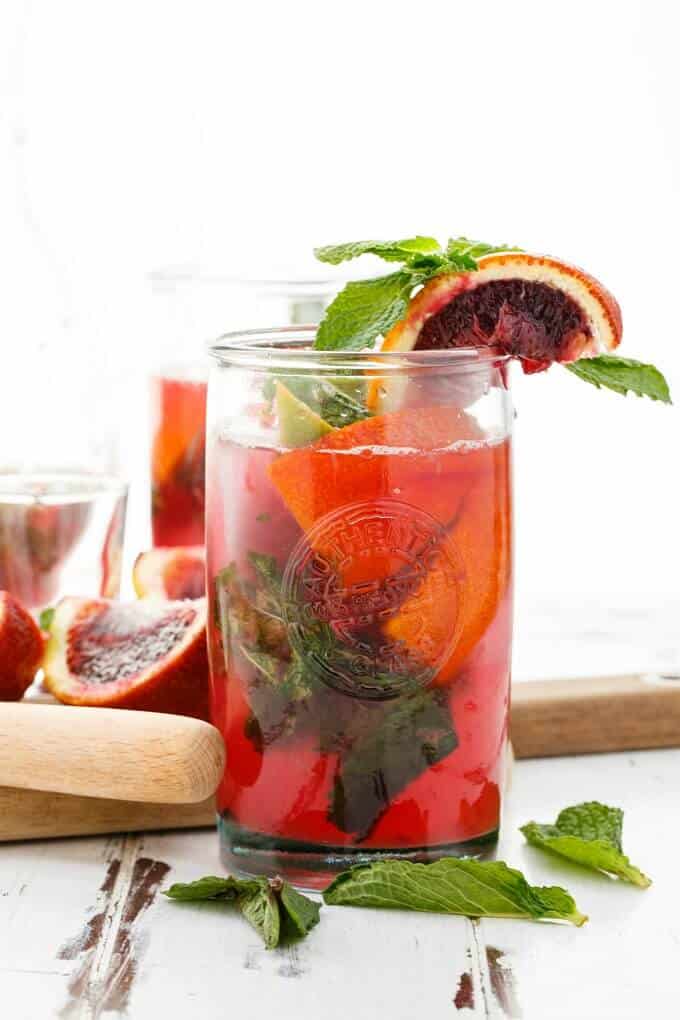 Blood orange mojito in glass cup with herbs. Ingredients in the background