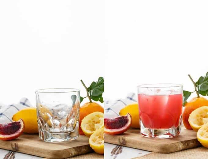 Blood Orange Whiskey Sour in glass cup with ice on wooden pad with lemons, oranges and cloth wipe.