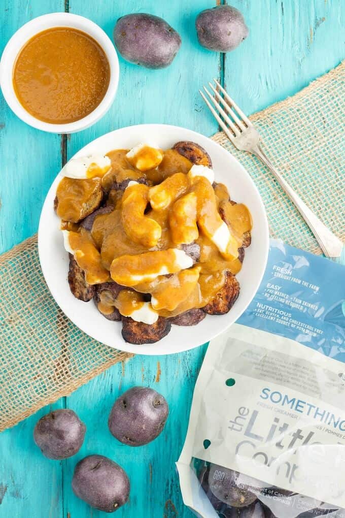 Grilled Potato Poutine  on white plate with fork, potaotes in sack and scattered around and bowl of sauce on blue table