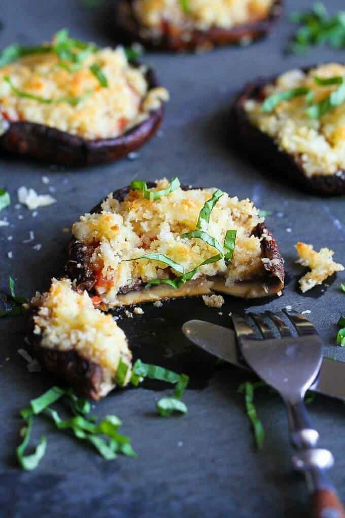 Roasted portobello mushrooms with cheese breadcrumb topping on black tray with fork and knife