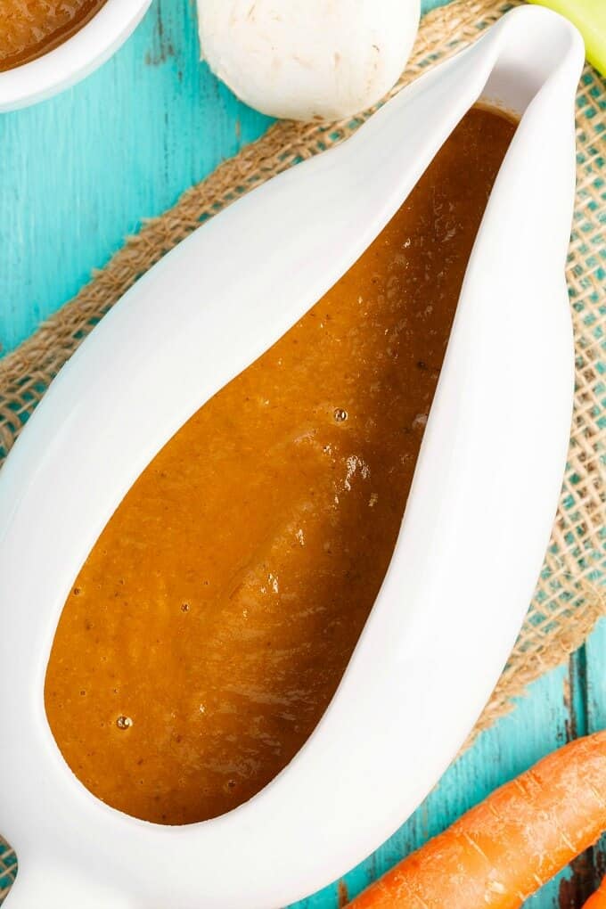 Vegetarian Mushroom Gravy  in white bowl with carrot and mushroom on blue table