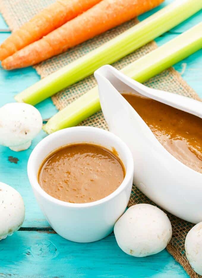 Vegetarian Mushroom Gravy  in white bowls with vegetable and mushrooms on blue table