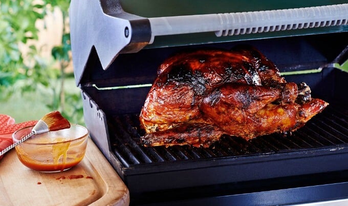 Whole turkey in grill next to table with bbq sauce and brush