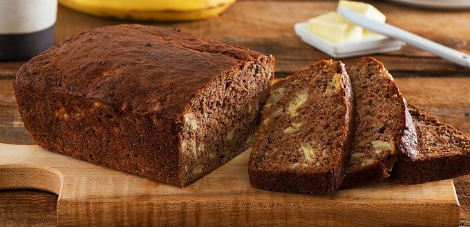 Chai spiced banana bread sliced on wooden pad. Butter and banana in the background