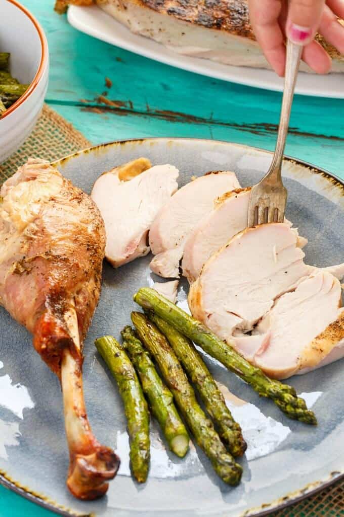 Grilled Spatchcock Turkey on blue plate with fork  held by hand and asparagus