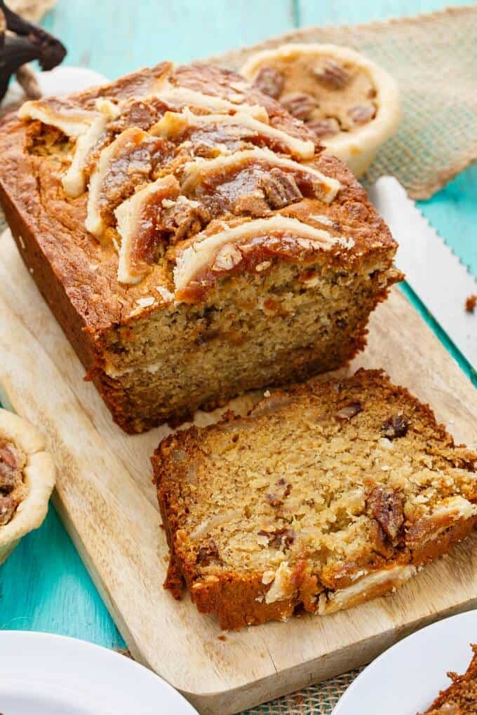 Homemade Butter Tart Banana Bread on wooden pad. Knife, white plates and small pies on blue table