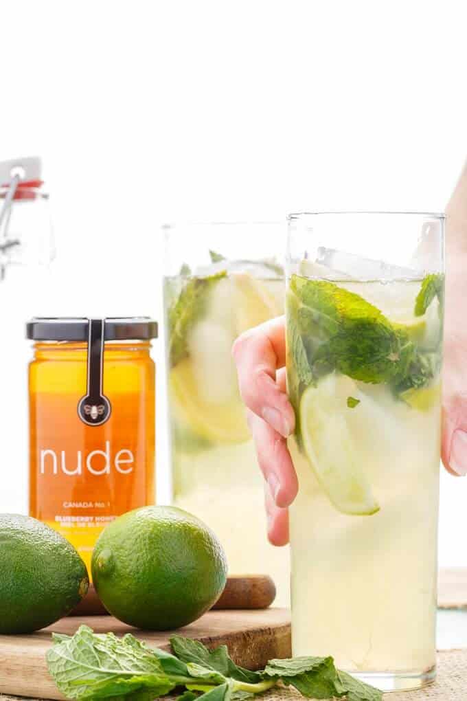 Homemade Honey Mojitos  in glass cups held by hand, jar of honey, limes and herb on wooden pad