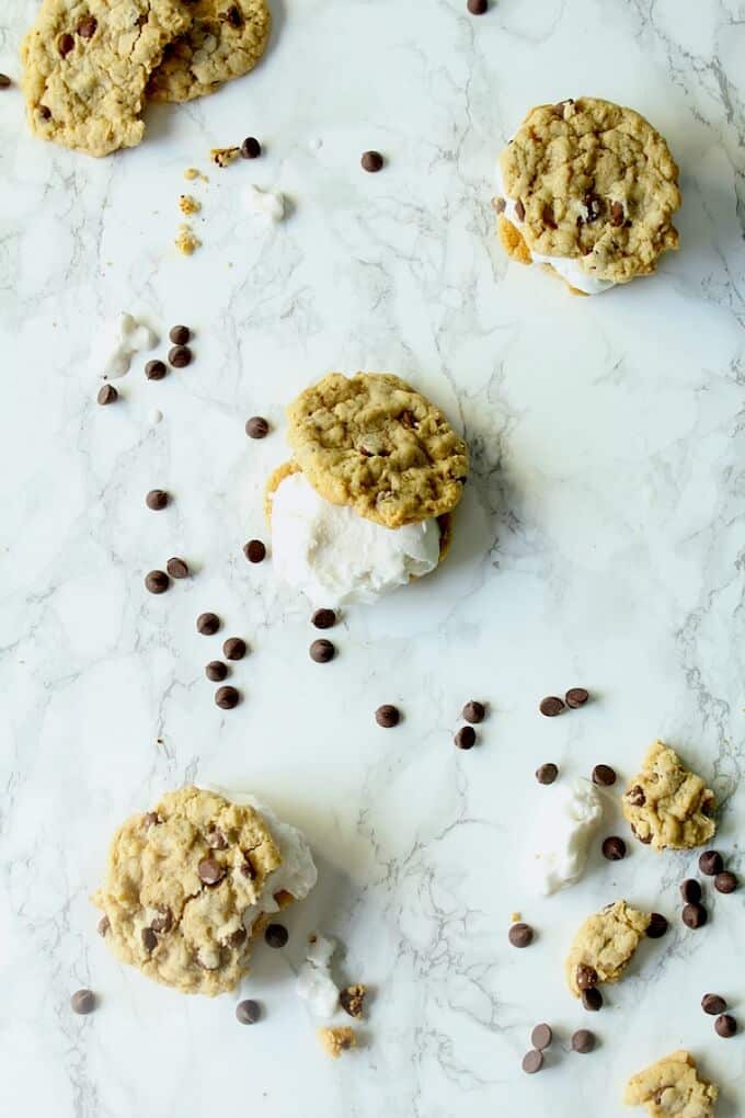 Chocolate chip cookie ice cream sandwiches on white-gray table with scattered chocolate chips