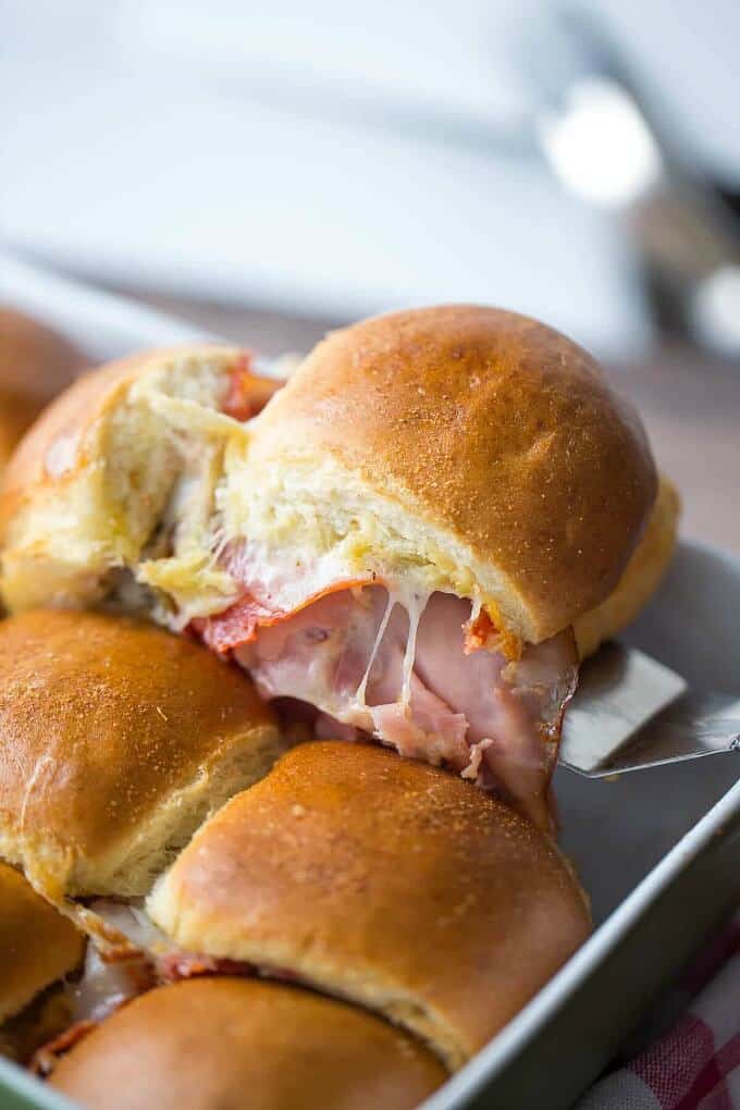 Hot italian party sandwiches on baking tray picked by spatula