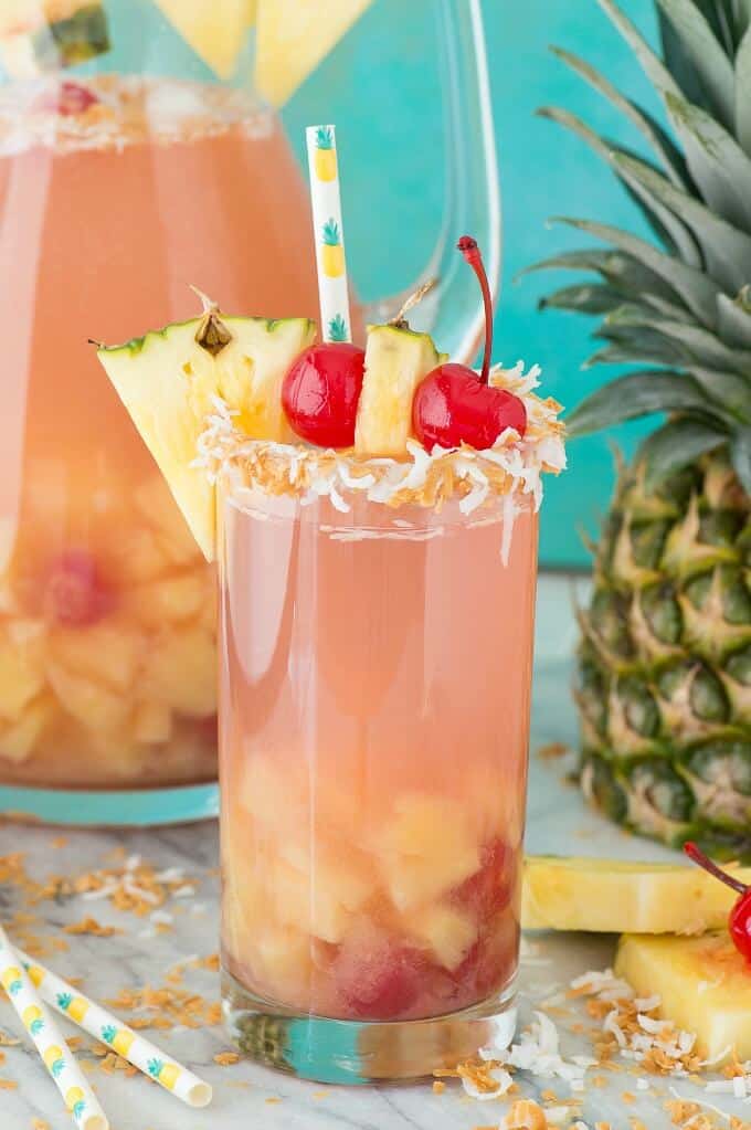 Pina colada sangria in glass cup with straw,pineapple slcies and cherries on the top. Pineapple, straw and glass pitcher on table