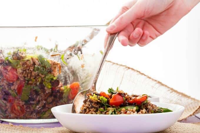 Roasted Mushroom Wild Rice Salad on white plate with spoon held by hand. Salad in big glass bowl  on table