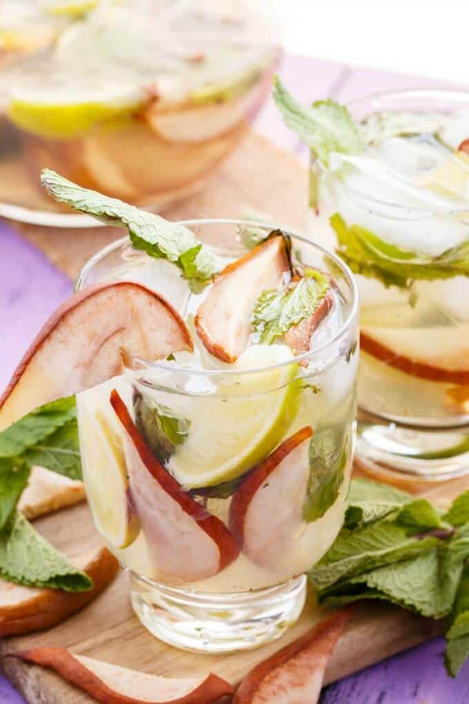 Roasted Pear Mojitos in glass cups on wooden pad with herbs and pear slices