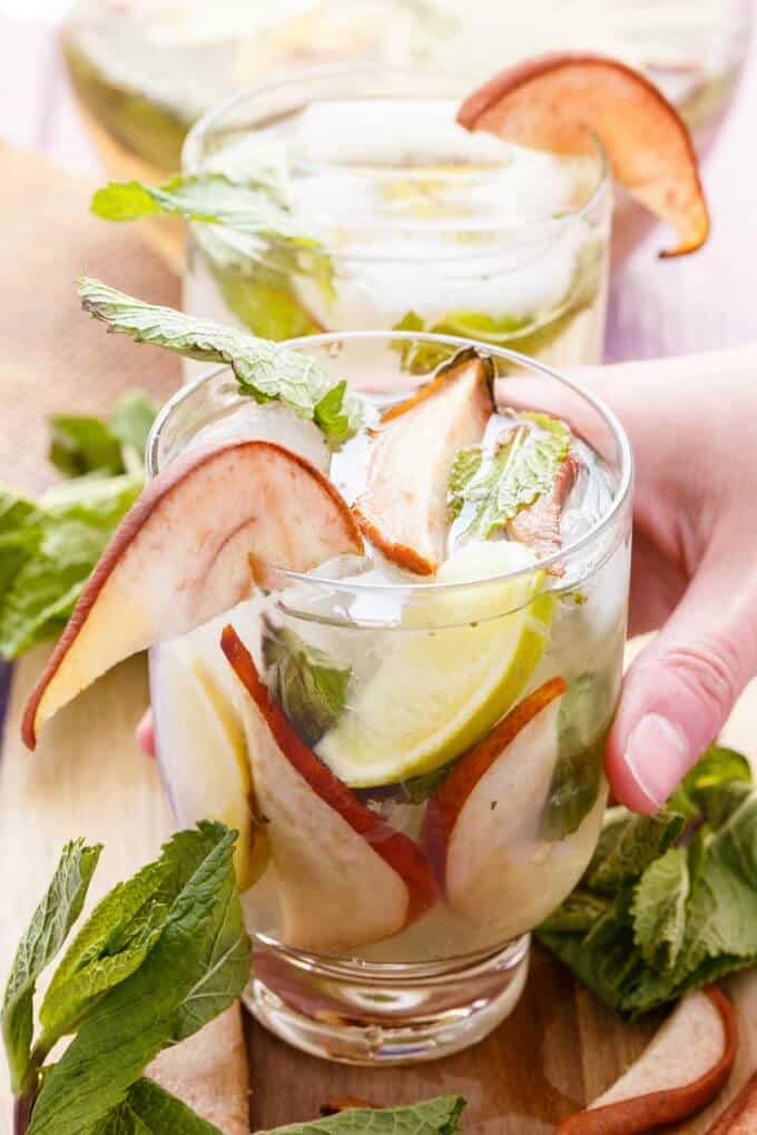 Roasted Pear Mojitos  in glass cup held by hand on wooden pad with herbs and roasted slices of pear