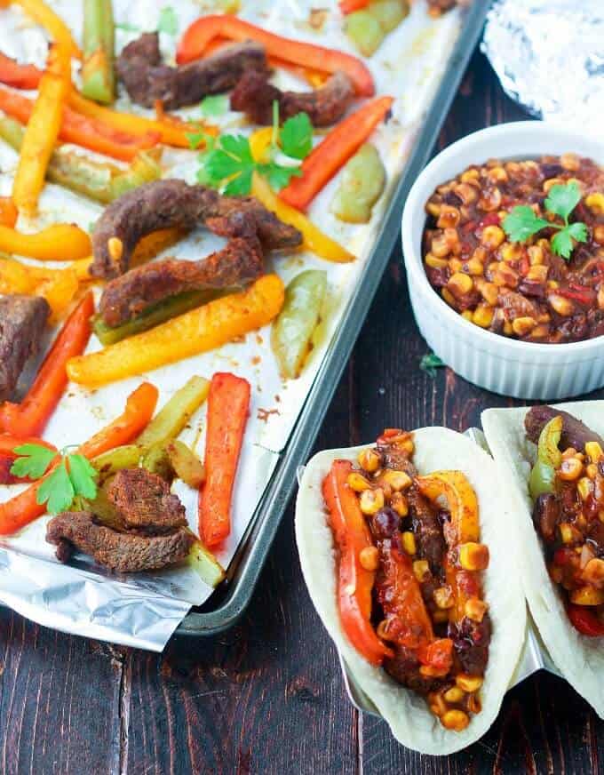 Sheet pan steak fajitas  on baking tray adn small plate, with bowl with sauce on table