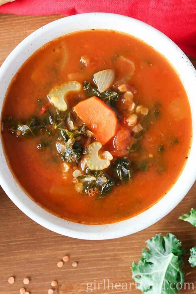 Spicy lentil soup with kale in white bowl. Scattered lentils and kale on brown table