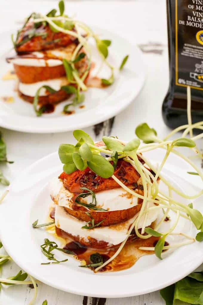 Tomato-Mozzarella Stacks  on white plates with herbs, balsamic vinegar in glass bottle in the background