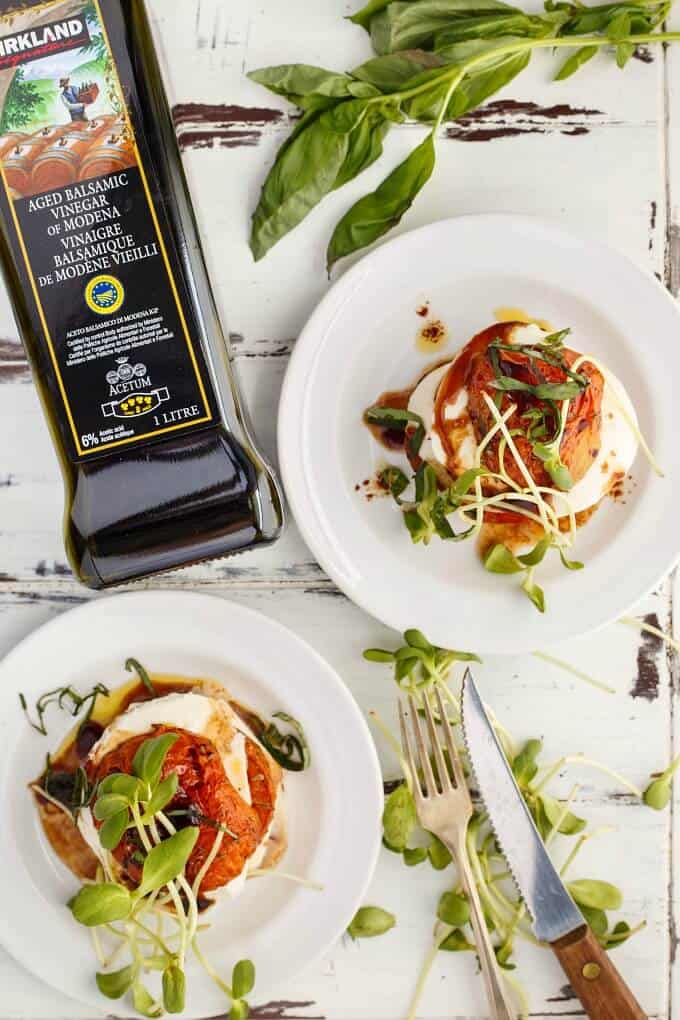 Tomato-Mozzarella Stacks  on white plates with herbs, Knife, fork, herbs and balsamic vinegar in glass bottle on the table