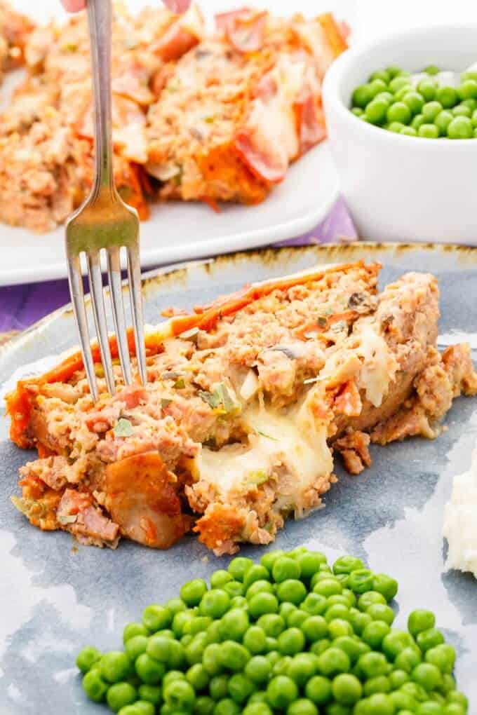 Turkey Pizza Meatloaf on blue plate with peas and fork. Bowl of peas and white tray with Turkey Pizza Meatloaf in the background