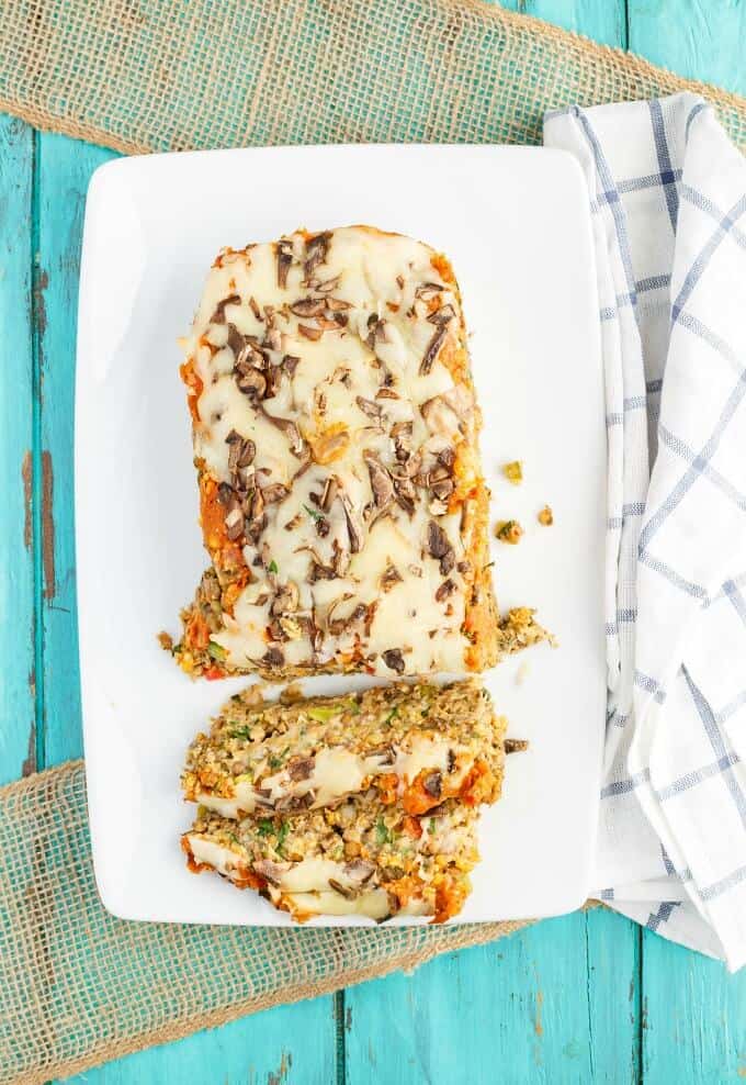 Vegetarian Pizza Meatloaf partially sliced on white tray on blue table with cloth wipe.