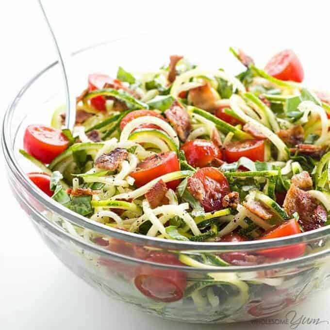 Zucchini noodle salat with bacon and tomatoes in glass bowl with fork